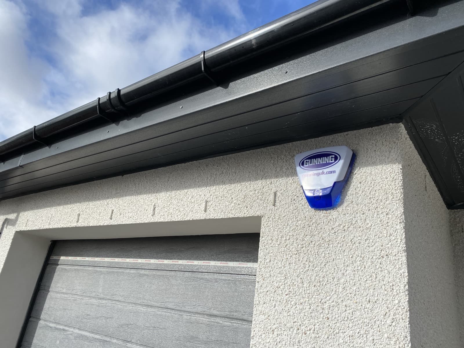 Branded Gunning alarm siren box mounted under the eaves of a new-build Lanarkshire home