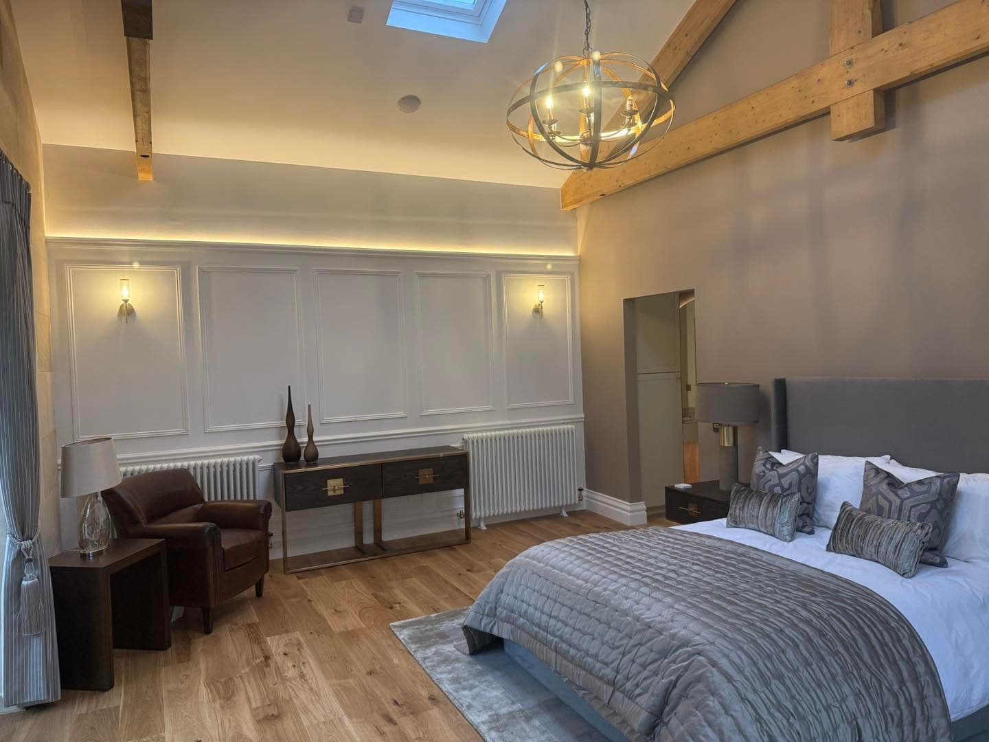 Vaulted master bedroom with cove lighting, wall sconces and a statement chandelier on exposed beams