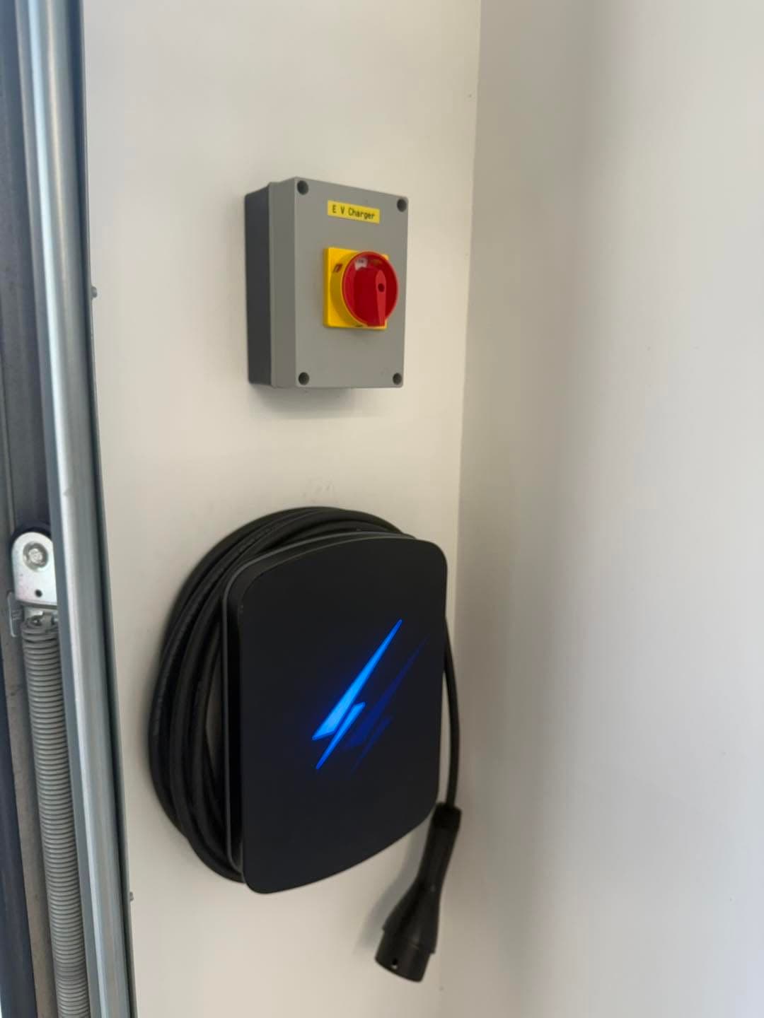 Black EV home charger with a red-and-yellow isolator switch mounted beside a garage door
