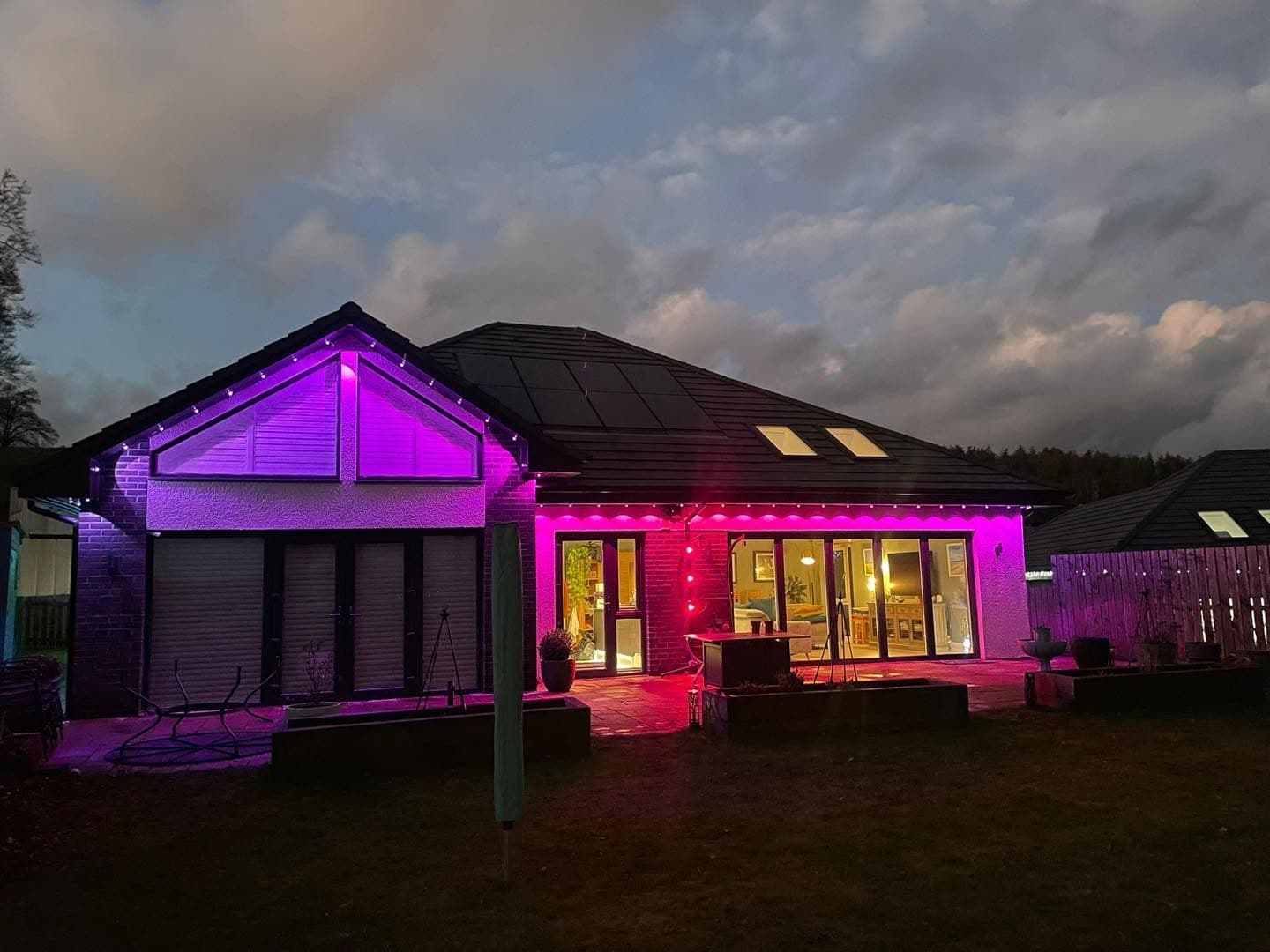 Detached house at dusk with colour-changing exterior LED lighting and solar panels on the roof